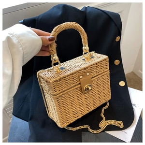 Detailed straw woven square handbag with gold metal clasp and chain strap held by a person