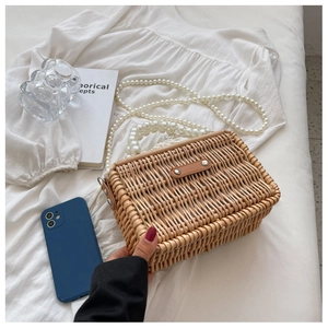 Detail view of straw woven bag featuring elegant pearl strap and leather buckle closure