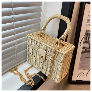 Detail of woven straw box bag featuring a gold metal twist lock and beige leather clasp