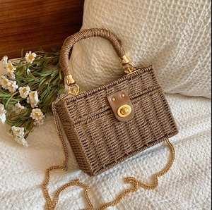 Vintage woven straw box bag with leather flap and gold chain strap on a soft background