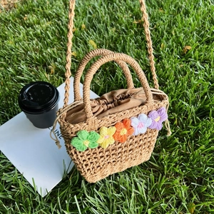 Mini floral woven straw handbag with colorful crochet flowers on a green lawn