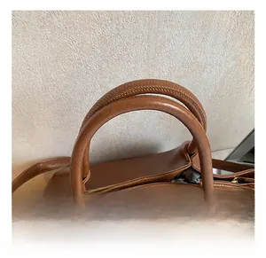 Gros plan sur la poignée en cuir marron avec boucle en métal doré et couture fine