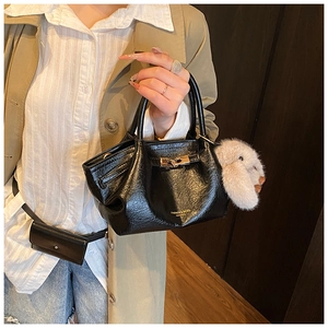 Détail du sac à main en cuir verni noir avec boucle dorée et breloque lapin en peluche