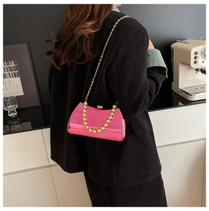 Detail of rose pink mirrored box bag featuring gold beaded handle and metal chain strap