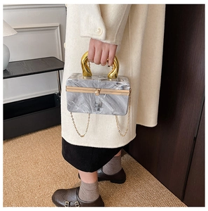 Detail of marble acrylic handbag with gold U-shaped handle and metal chain strap