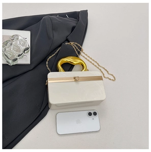 Detail of white acrylic clutch bag featuring a unique wavy gold handle and chain strap