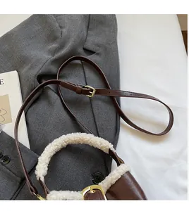Détail du sac seau en cuir marron foncé avec anse en fausse fourrure blanche et sangle
