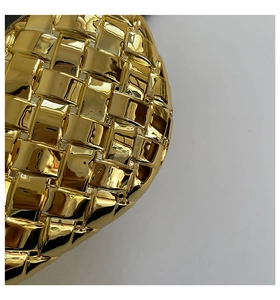Detail view of the intricate gold woven texture and metallic acrylic surface on the evening bag