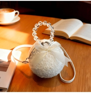 Detail of white plush spherical bag with beaded handle and large satin bow on wood desk