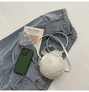 Close-up of white plush ball-shaped bag with beaded handle and silk bow detailing