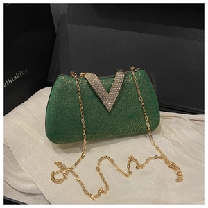 Macro shot of dark green evening clutch with gold V-shape buckle and fine metal chain