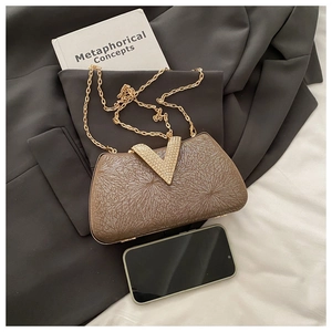 Detail of evening clutch with V-shaped diamond buckle and chain strap next to a phone