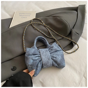 Détail du sac à bandoulière en denim bleu en forme de nœud avec motif matelassé et chaîne