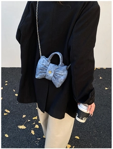 Sac bandoulière en denim bleu avec nœud et bouton fleur dorée porté à l'épaule