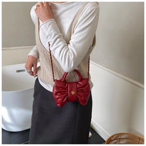 Détail du sac à main nœud rouge avec texture matelassée et fleur centrale dorée
