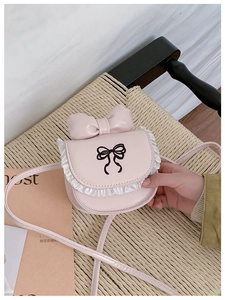 Detailed view of pink crossbody bag with lace trim and embroidered bow on woven chair