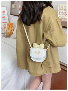 Detail of white mini crossbody bag with yellow bow and lace trim worn by a child girl