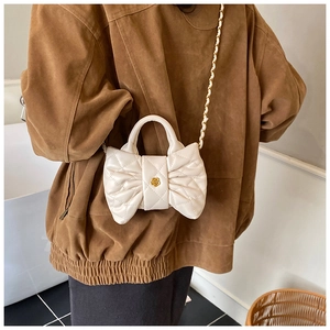 Détail d'un sac nœud blanc matelassé avec boucle fleurie dorée et bandoulière chaîne