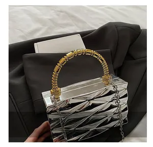 Close-up of a silver acrylic box bag with 3D ripples and a gold beaded top handle