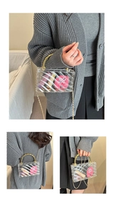 Detail of transparent acrylic box bag with golden spiral handle and metal chain strap