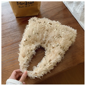 Top view of a fluffy cream faux fur bucket bag with gold sequins on dark wood table