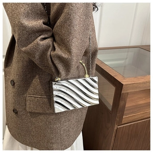 Detail of silver wavy acrylic clutch bag with metal handle and chain shoulder strap