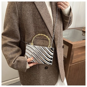Detail of silver wavy texture acrylic evening bag with gold bamboo handle and chain strap