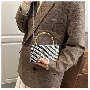 Detailed view of silver acrylic box bag with 3D wave texture and gold beaded handle