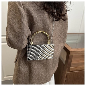 Detail of evening bag with metallic wave pattern held by model in brown tweed blazer