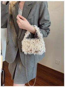 Close-up of a cream-white plush bucket bag with sequins and silver chain strap on a model