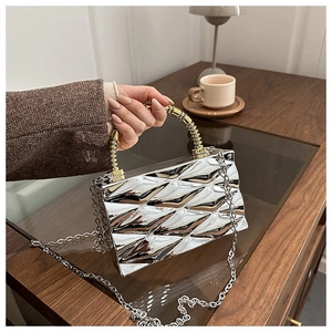Close-up of a silver diamond-pattern acrylic box bag with gold spiral handle on a table
