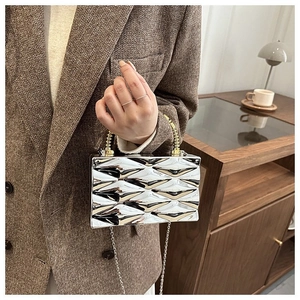 Detail of silver metallic box bag showing textured rhombic pattern and gold bead handle