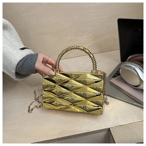 Detailed view of gold geometric acrylic clutch bag with bead handle on a wooden desk