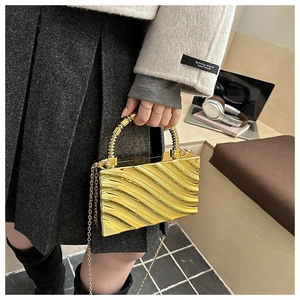 Detail showing the golden acrylic box bag with wavy texture and spiral metal handle
