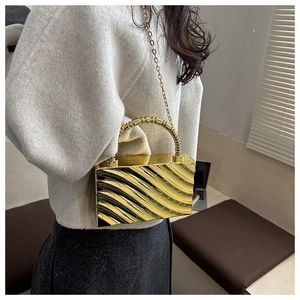 Detail of golden acrylic box bag featuring textured wave pattern and beaded metal handle
