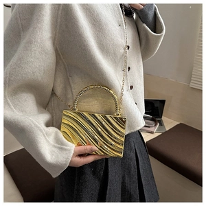 Close-up of golden evening box bag with wave texture, round handle and chain strap