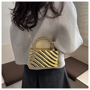 Macro detail of golden acrylic box clutch showing wavy texture and metal handle