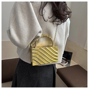 Chic gold acrylic box bag with wavy texture shown on a shoulder in a cafe setting
