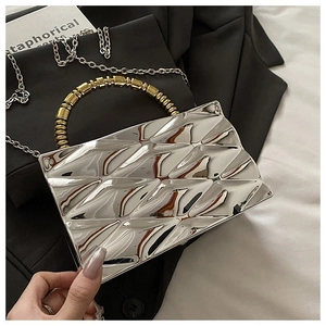 Detail of silver geometric clutch with gold beaded handle and metal chain on a suit