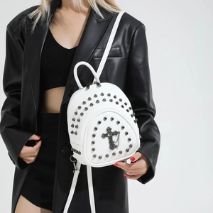 White vintage mini backpack with metallic studs and cross pendant worn by model