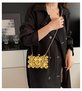 Golden egg-shaped evening bag with metallic studs and chain strap on black trench coat