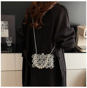Detail of transparent spherical shoulder bag with metallic chain strap worn by a model