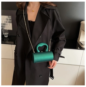 Détail d'une pochette cylindrique en acrylique vert foncé avec chaîne et poignée dorée