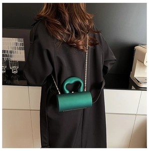 Détail du sac cylindrique vert foncé en acrylique avec bandoulière dorée sur trench-coat