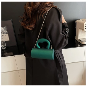 Pochette cylindrique en acrylique vert foncé avec chaîne dorée portée par un mannequin