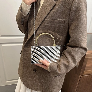 Silver wavy acrylic box clutch with a gold spiral handle shown on a model outfit