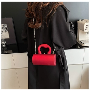Détail du sac de soirée cylindrique rouge avec poignée incurvée et bandoulière en chaîne dorée