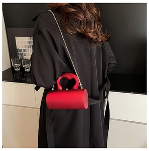 Détail d'une pochette cylindrique rouge avec poignée cœur et chaîne dorée sur manteau