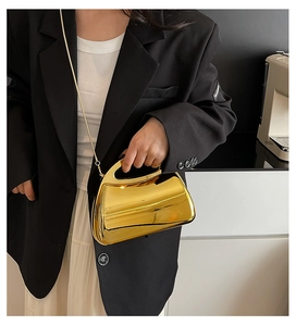 Detail of a structured gold mirrored acrylic handbag with ergonomic handle and chain