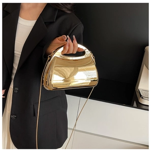 Close-up of golden mirrored acrylic handbag with curved handle and metal chain strap